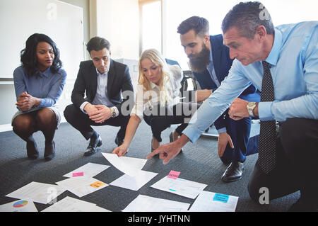 Il team di Business guardando le carte sul pavimento con manager che puntano a una idea Foto Stock