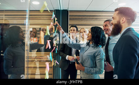 Felice imprenditori creativi di brainstorming in office, mettendo sticky notes con idee su vetro Foto Stock
