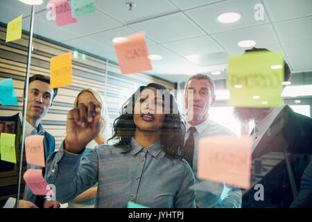 Gruppo di imprenditori il brainstorming con la donna in primo piano, mettendo una nota adesiva sul vetro Foto Stock