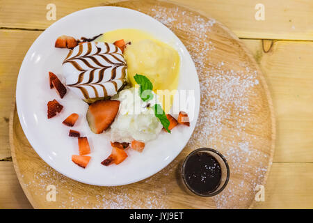 Deliziosi pancake con fragole e gelato alla vaniglia con topping di cioccolato e panna montata su sfondo di legno Foto Stock