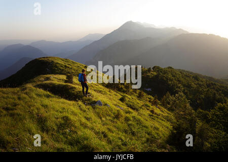 Donna in piedi sulla cima di una montagna al tramonto e godendo della vista panoramica sulle Alpi, Slatnik, Slovenia. Foto Stock