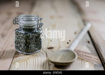 Spice in un recipiente su un tavolo di legno, il cucchiaio di legno, sfondo nero Foto Stock