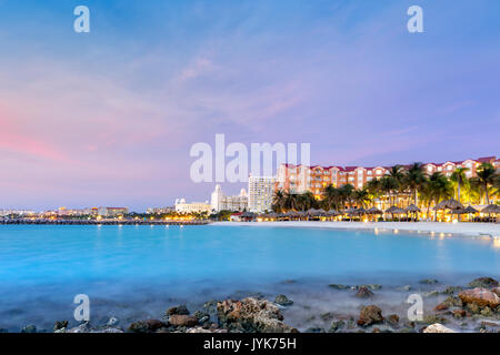 Alto hotel area in Aruba al crepuscolo. Le palme in movimento suggeriscono il tempo ventoso, una ben nota caratteristica di questa isola, situata sul sout Foto Stock