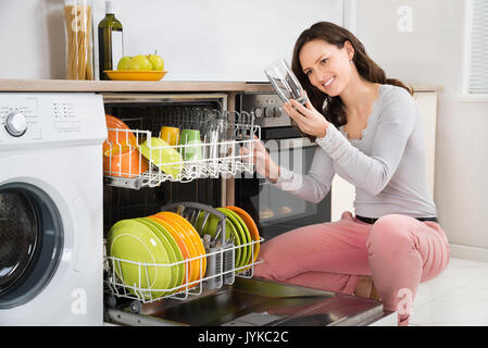 Giovane bella donna prendendo bicchiere dalla lavastoviglie in cucina Foto Stock