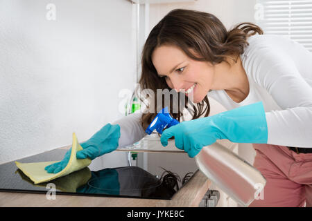 Giovane donna sorridente durante la pulizia del piano di cottura ad induzione sul bancone a casa Foto Stock