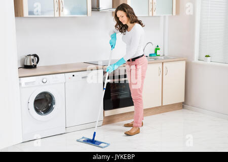 Donna felice pulizia pavimento con Mop in cucina a casa Foto Stock