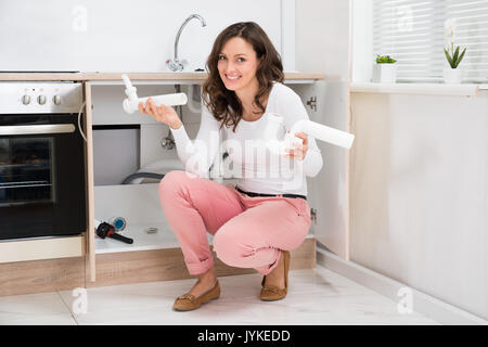 Giovane donna accovacciata sul pavimento con la fogna tubo in plastica in cucina Foto Stock