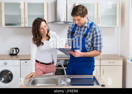 Felice donna in piedi con giovani Plumber iscritto negli appunti in cucina Foto Stock