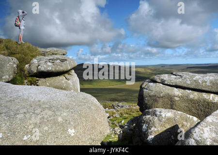 Un camminatore o escursionista in piedi in cima a una roccia a ruvida tor su Bodmin Moor in North Cornwall Tourism scenario viste drammatiche da solo nella parte superiore Foto Stock