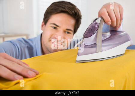 Ritratto di giovane uomo di piegatura e stiratura T-shirt con ferro da stiro elettrico in cucina Foto Stock