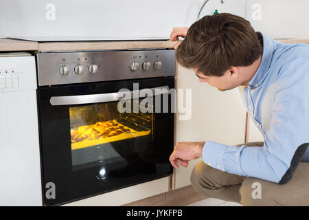 Giovane uomo la cottura del pane nel forno apparecchio a casa Foto Stock