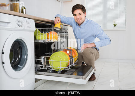 Giovane uomo felice disponendo i piatti in lavastoviglie in cucina moderna Foto Stock