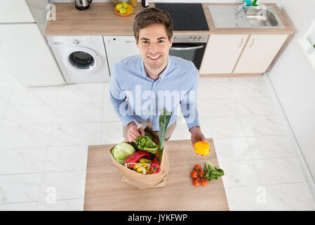 Elevato angolo di visione dell uomo la rimozione di verdure dal sacchetto di generi alimentari in cucina Foto Stock