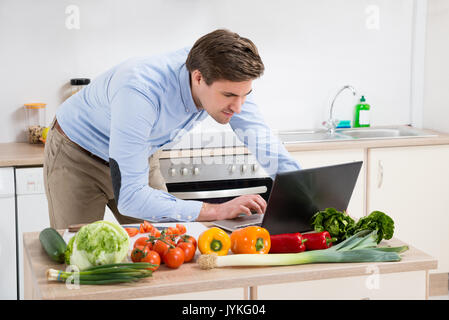 Giovane uomo Cerca ricetta su laptop in cucina a casa Foto Stock