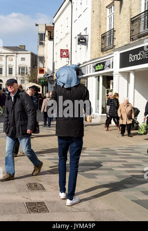 Alto uomo camminare per high street in Inghilterra di trasportare un bambino sulle spalle durante il giorno con gli altri acquirenti in background Foto Stock