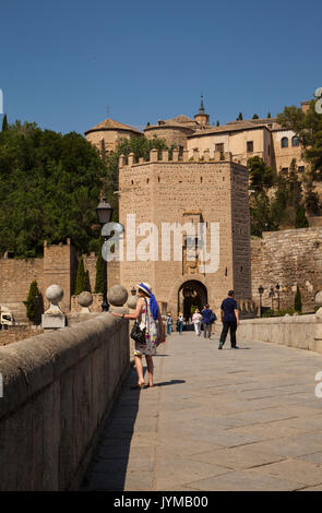 I turisti a piedi oltre l'Alcantara ponte sopra il fiume Tago verso la città medievale di Toledo Spagna con l'Alcazar in background Foto Stock