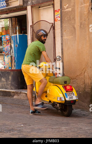 Uomo di salire sul giallo scooter indossare pantaloncini giallo e verde tee shirt a Toledo Spagna Foto Stock