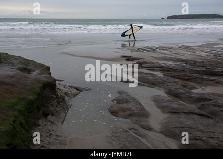 Surfista maschio in muta passeggiate lungo il Rocky Waters Edge portante della tavola da surf Foto Stock