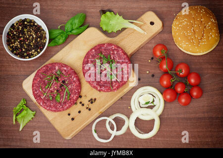 Vista dall'alto di due materie hamburger, pomodori e cipolla sulla tavola di legno Foto Stock