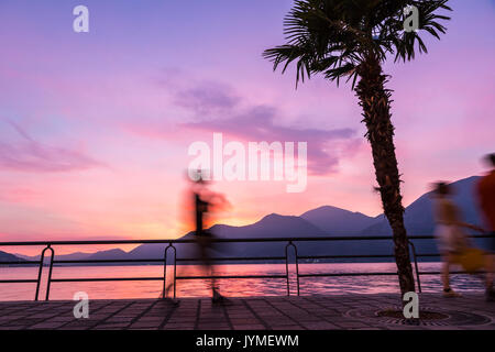 Il pittoresco foggy tramonto al lago d'Iseo, Lombardia, Italia. Sagome di persone che camminano sulla passeggiata a mare street nella città di Iseo Foto Stock