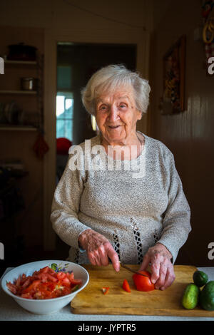 Una donna anziana trita verdure per insalata in cucina. Foto Stock