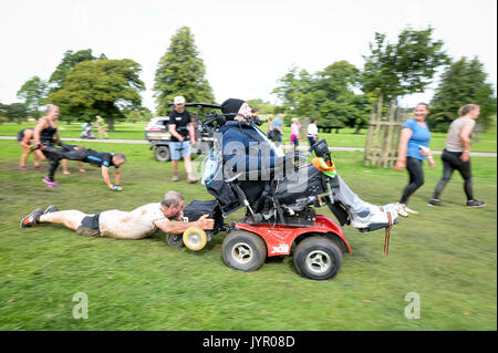 Rob Camm, che soffre da tetraplegia e paralised dal collo in giù, trascina il suo papà Ian in un 'carriola' ostacolo come egli prende parte alla sua terza dura Mudder evento al Badminton station wagon, Wiltshire, dove egli è affrontare il corso con un appositamente progettato sedia egli controlla con il suo mento. Foto Stock