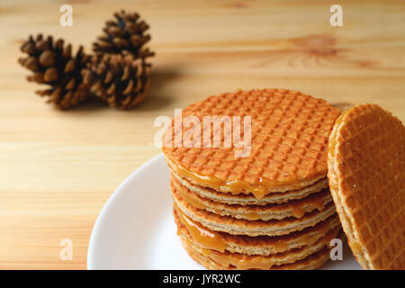 Impilati Stroopwafel sulla piastra bianca servita su un tavolo di legno con sfocato Pigne in background Foto Stock