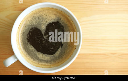 Forma di cuore caldo caffè nero schiuma, vista dall'alto con spazio libero sul tavolo di legno per testo e design Foto Stock