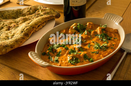 Close up di servire un piatto di pollo al curry con pane naan e una bottiglia di vino rosso sul tavolo in legno di quercia Foto Stock