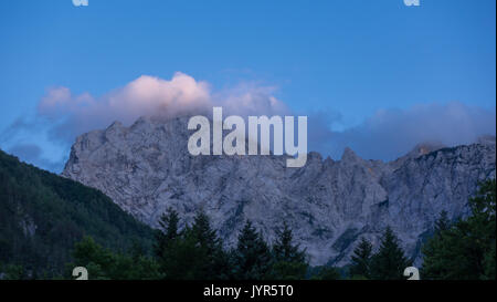 Alpini a picco nel tramonto sul cielo blu e nuvole e le foreste in primo piano, logarska valle di Logar, slovenia Foto Stock