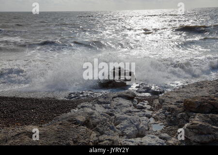 Onde che si infrangono sulla marea sulla costa del Galles con il sole si riflette sulle acque di increspatura Foto Stock