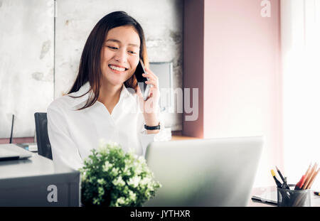 Asian imprenditrice parlando al telefono mobile nella parte anteriore del computer portatile in ufficio,Ufficio concetto di stile di vita. Foto Stock