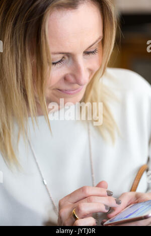 Giovani capelli biondi business donna la scrittura di un messaggio di testo utilizzando Messenger sul telefono cellulare. Candide unposed ritratto. Orientamento verticale Foto Stock