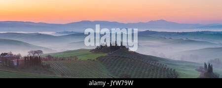 Valdorcia, Siena, Toscana, Italia. Vista panoramica di una fattoria toscana situata sulla sommità di una collina a sunrise. Foto Stock