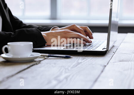 Uomo al lavoro su un computer portatile su una tavola in legno rustico, mani vicino fino Foto Stock