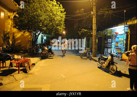 Locale notturno uomo vietnamita rilassante mentre manning negozio vendita ornamenti da strada, turisti in bicicletta pedalando nel locale di uomini vietnamita r Foto Stock
