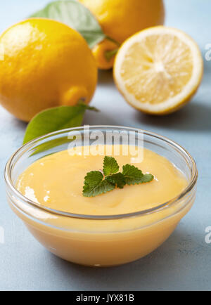 Cagliata di limone in una ciotola di vetro, limoni freschi su uno sfondo blu Foto Stock