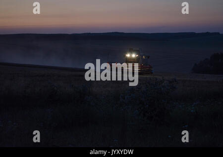 Vendemmia notturna, mietitrebbiatrici stanno raccogliendo su un campo di grano. Foto Stock