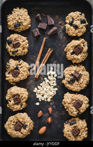 Vista superiore del pane appena sfornato, fiocchi d'avena raisin cookies con cioccolato fondente, la cannella e i dadi sul vecchio arrugginito cookie foglio. Foto Stock