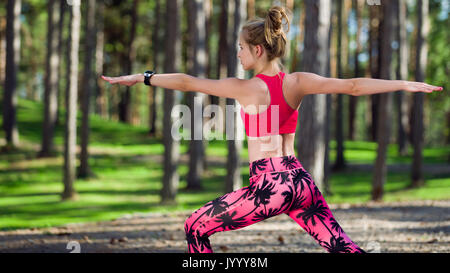 Giovane donna a praticare yoga in una foresta. Posa del guerriero. Il Calmness, relax del corpo e della mente il concetto di felicità Foto Stock