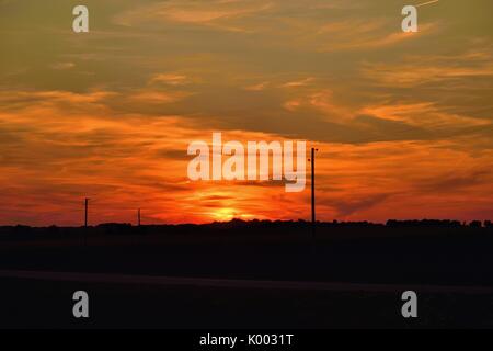 Burlington, Illinois, Stati Uniti. Bagliore dal sole che tramonta visibile oltre le linee telefoniche rurali. Foto Stock