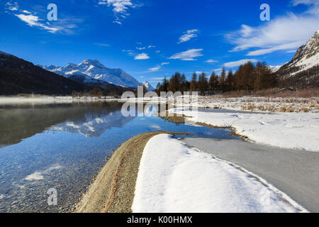 Vette innevate sono riflesse nel lago di Silvaplana ancora parzialmente congelato Maloja Cantone dei Grigioni Engadina Svizzera Europa Foto Stock