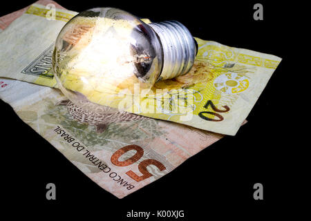 Due brasiliane denaro reale note, di 50 e 20 Valore, moneta del Brasile, su uno sfondo nero e una luce accesa la lampadina sulla parte superiore, come un idea di denaro e di concetto Foto Stock