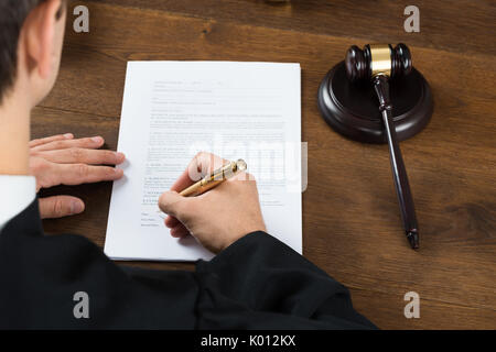 Angolo di alta vista del giudice maschio sulla scrittura di documenti legali al banco nelle aule di tribunale Foto Stock