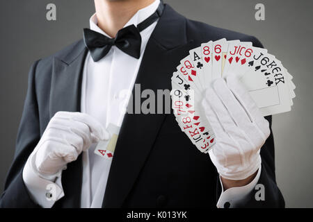 Sezione mediana del mago che mostra ventaglio carte contro uno sfondo grigio Foto Stock