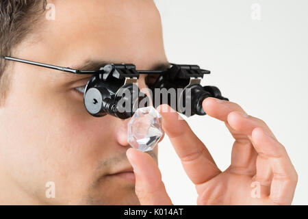 Vista dettagliata del gioielliere esaminando il diamante con la lente di ingrandimento contro uno sfondo bianco Foto Stock