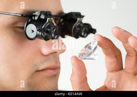 Vista dettagliata del gioielliere esaminando il diamante con la lente di ingrandimento contro uno sfondo bianco Foto Stock