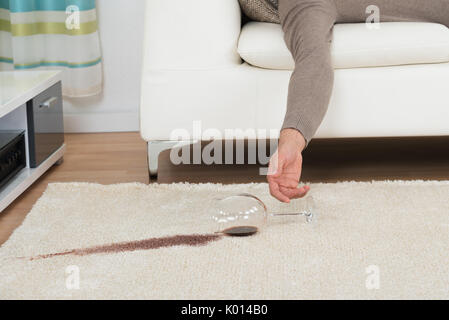 Ritagliate la mano di uomo ubriaco fuoriuscita di vino rosso sul tappeto a casa Foto Stock