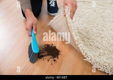 Elevato angolo di visione dell'uomo utilizzando la spazzola per spazzare via il fango sul pavimento di legno a casa Foto Stock