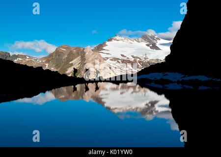 Sagome di escursionisti sulla riva del lago glaciale vicino al rifugio Marinelli. Sullo sfondo del ghiacciaio , Scerscen Valmalenco, Lombardia, Italia Foto Stock